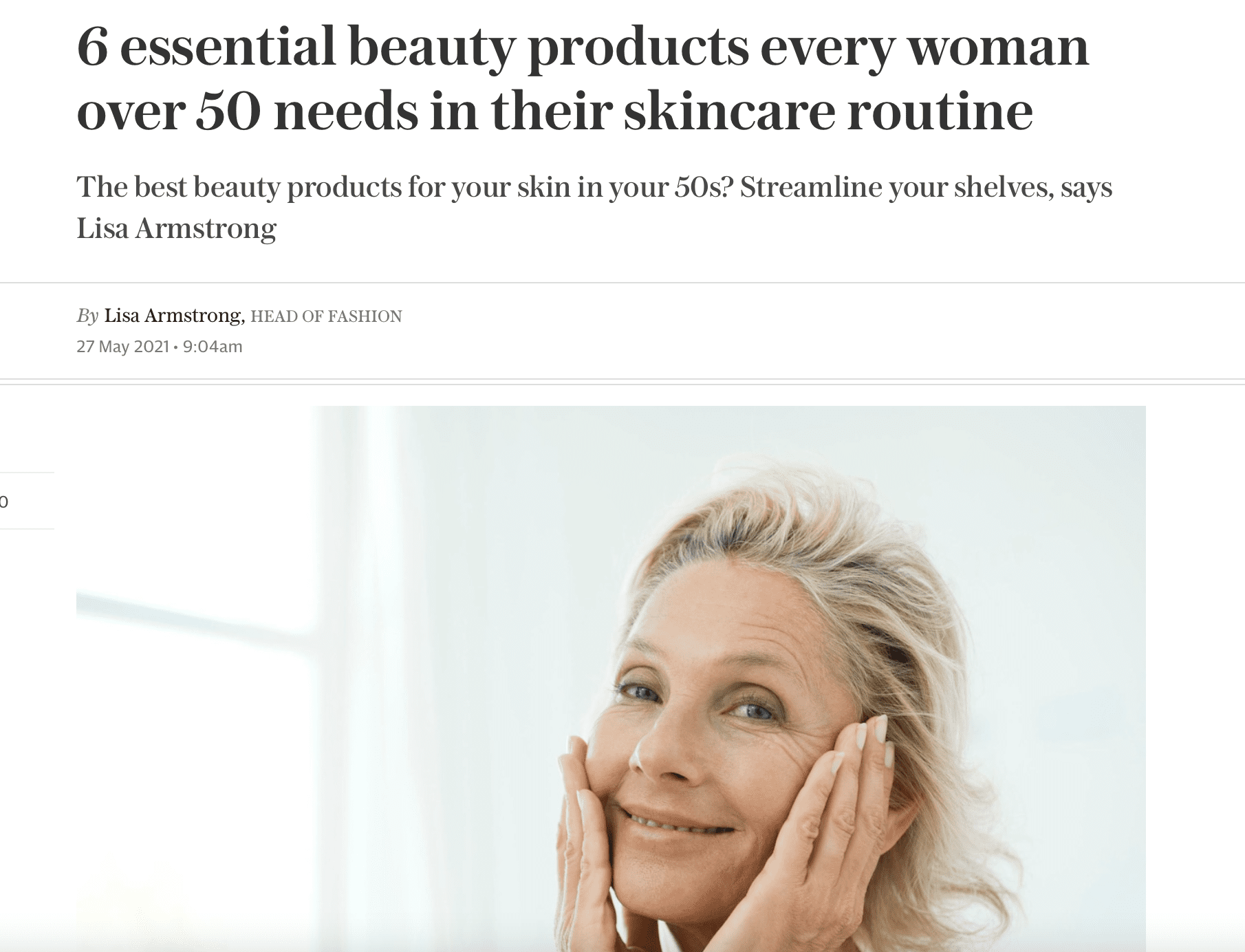 A smiling older woman with fair hair touches her face gently with both hands. She stands against a plain background, promoting skincare for women over 50, as described in the article headline above her.